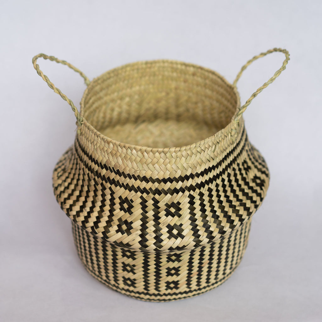 Handwoven palm fiber belly basket in traditional Oaxacan designs. Tan and black vertical stripes alternate with two vertical rows of small squares in each quarter of the basket.  Horizontal stripes run along both top and bottom edge Interior of basket is natural tan. Gray background.