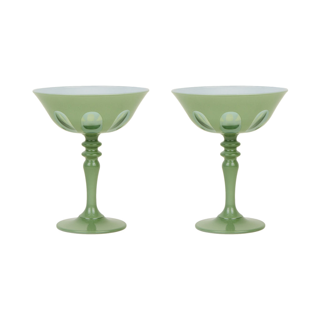 Pair of light green toned tall handblown curvy glasses. Skinny stem with a round base topped with a curved bowl with a mix of opaque and transparent arches. White background.