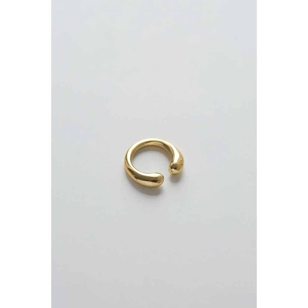 Brass open ring with curvy ends that don't quite meet. Light gray background.