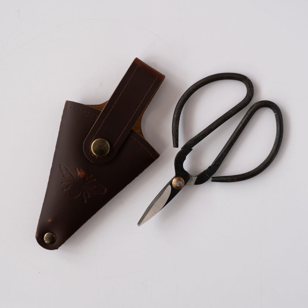Wide handled small scissors with leather pouch with an engraved bee on it. White background.