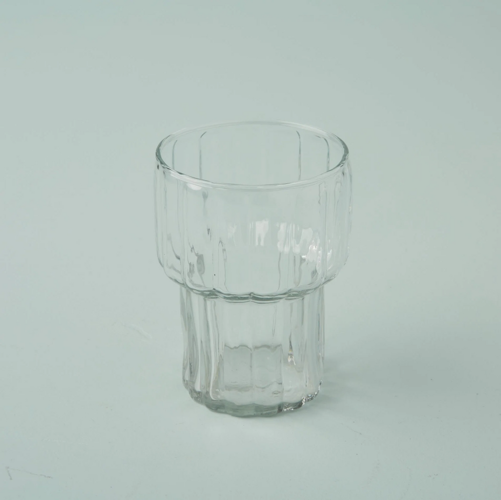 Ribbed texture handblown drinking glass that curves out at the halfway point. Sitting on an aqua background.