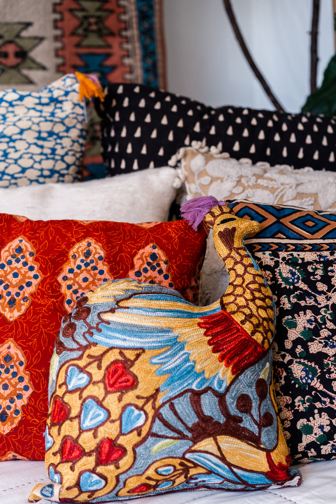 A brightly colored peacock shaped pillow. Orchid, maroon, red, light blue, turquoise, gold.