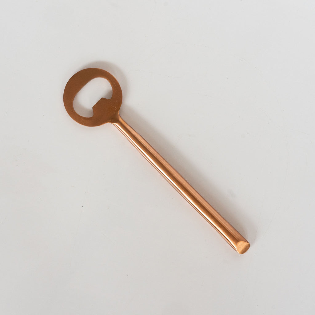One matte copper metal bottle opener on a white background.