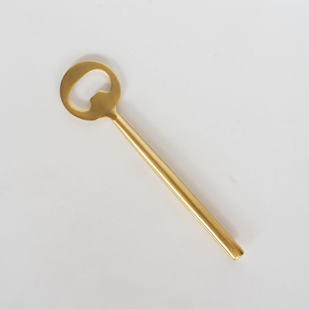 One matte gold metal bottle opener on a white background.