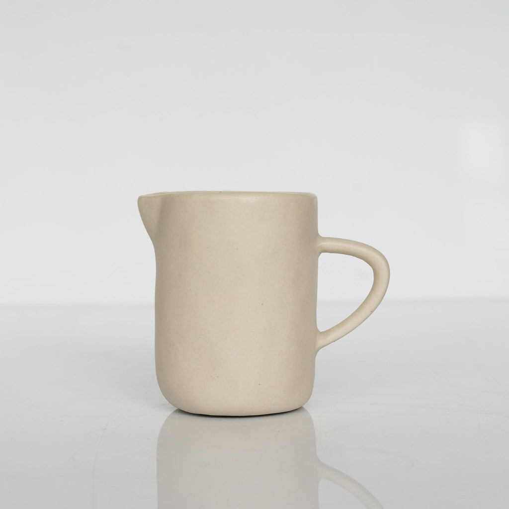 Small stoneware creamer jug with skinny handle on a white background.