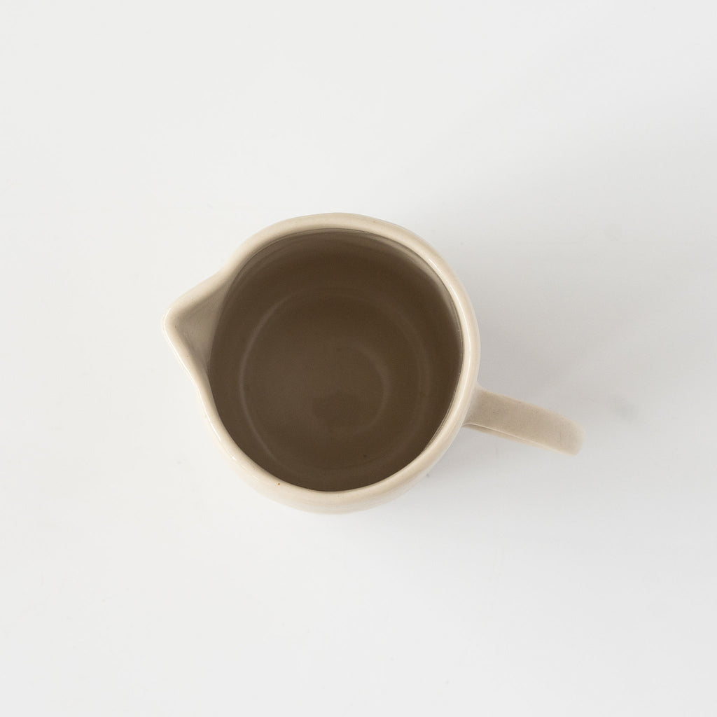 Top view of small stoneware creamer jug with skinny handle on a white background.