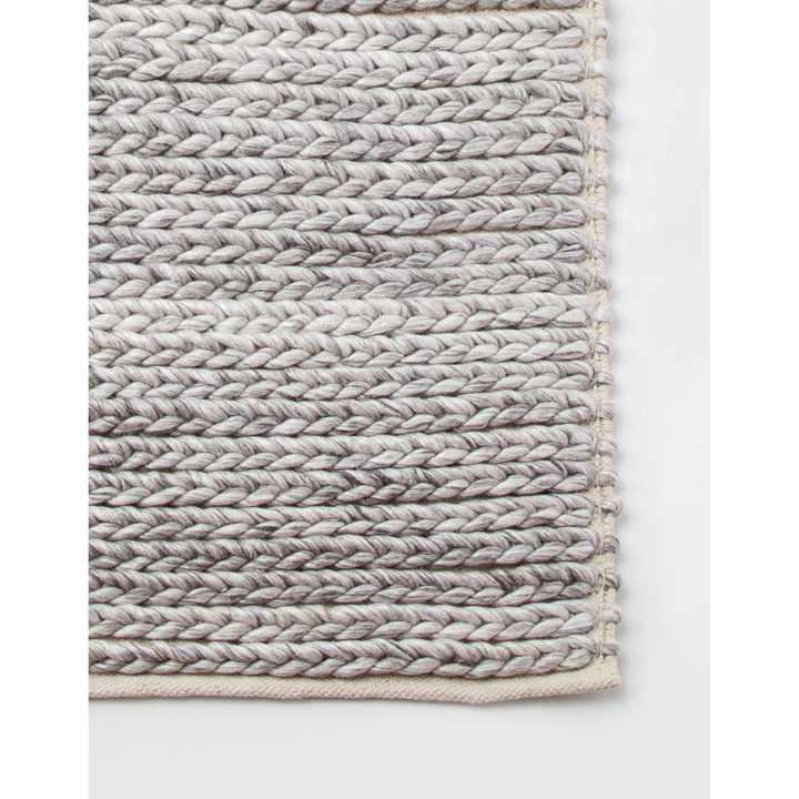Braided charcoal toned wool knitted rug on white background. 