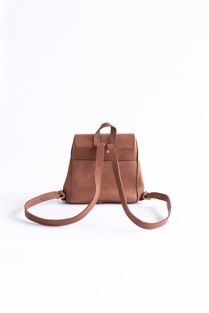 The back of a vegetable tanned brown leather small backpack sits on a white background. Hanging loop and adjustable straps are shown.