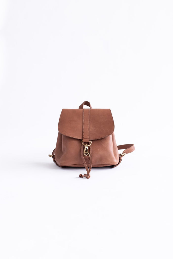 Vegetable tanned brown leather small backpack with gold clasp hardware sits on a white background.