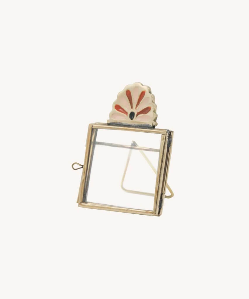 Small brass frame with simple border and a pink and brass art deco petal fan on top. White background.