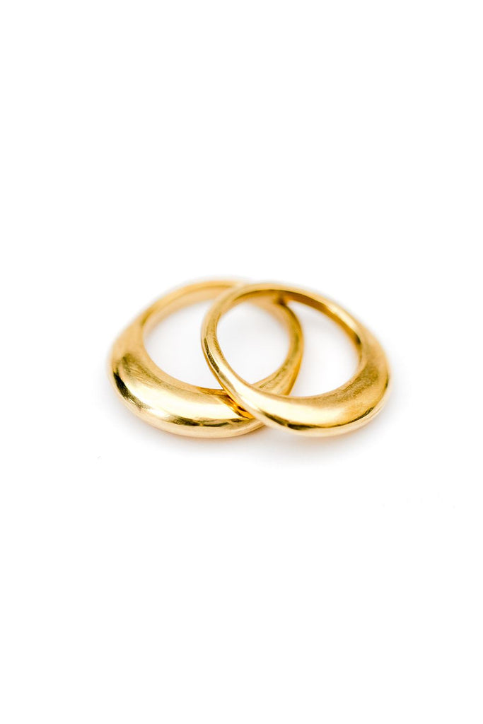 Two brass rings that are wider on the top are stacked offset on a white background.