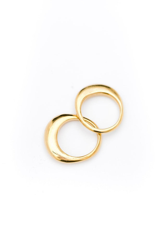 Two brass rings that are wider on the top are laying together on a white background.