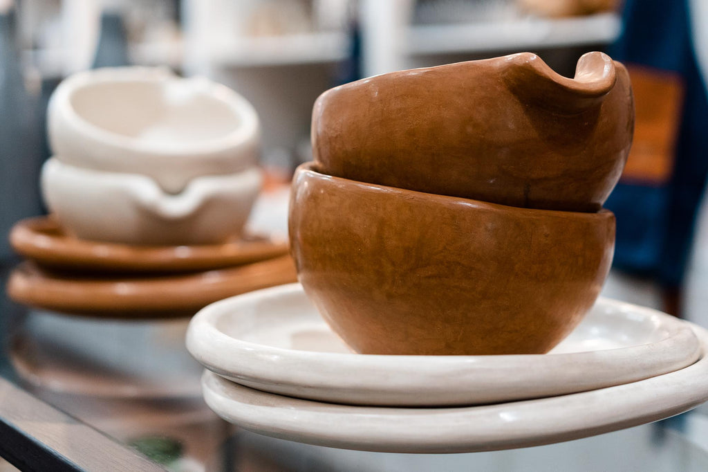 Two Tadelakt terra cotta toned bowls with pouring spout are stacked on two white Tadelakt plates / trays. In the background, two white terra cotta bowls with pouring spout sit on top of two terra cotta toned Tadelakt trays / plates.
