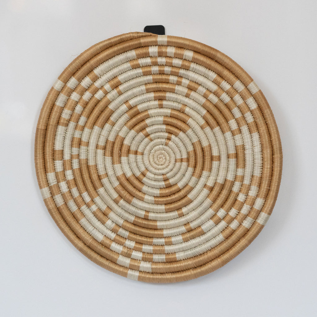 Handwoven Rwandan sweetgrass trivet with a cream flower design on tan. White background.